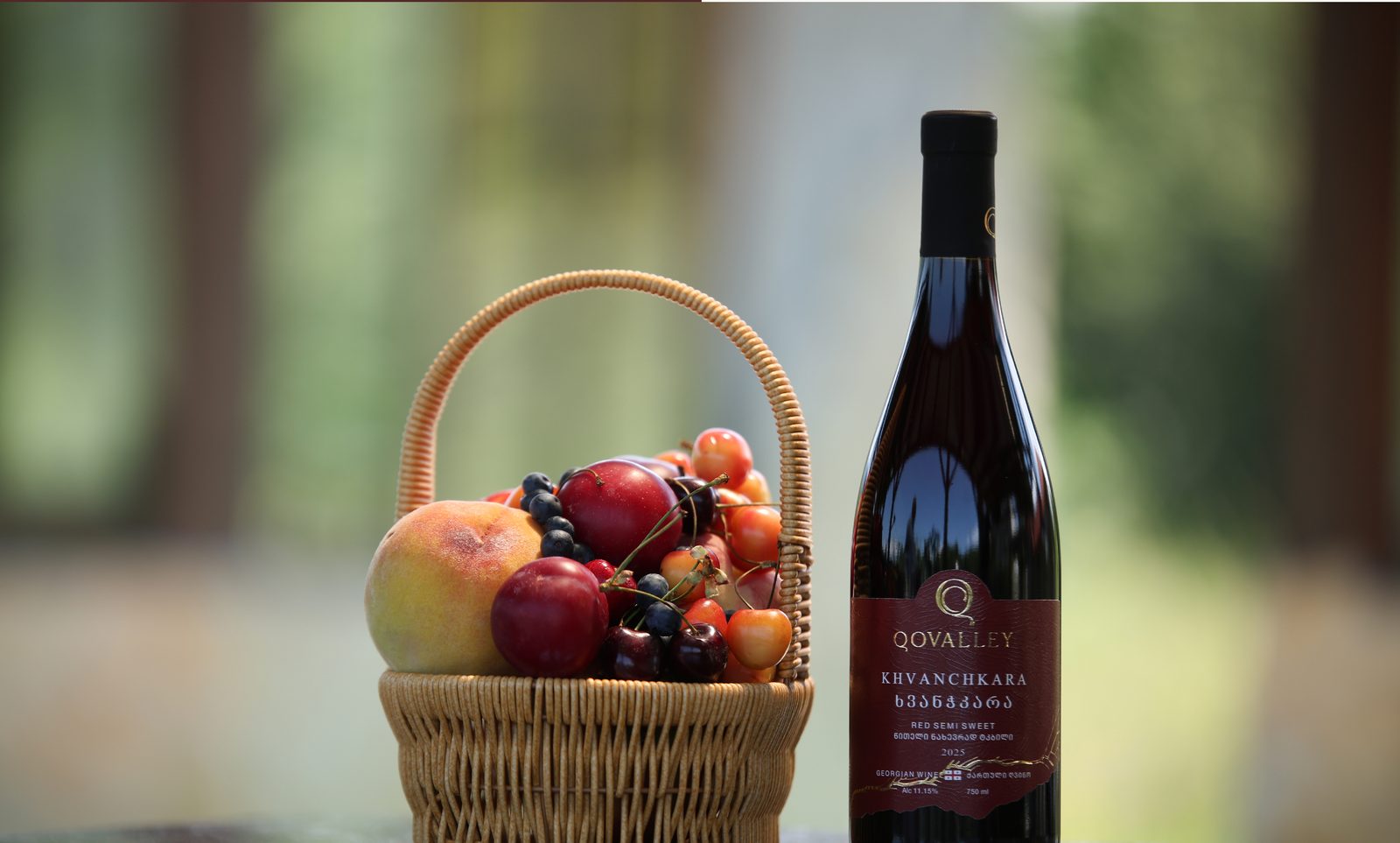 A basket of fruit beside a bottle of Qovalley Khvanchkara
